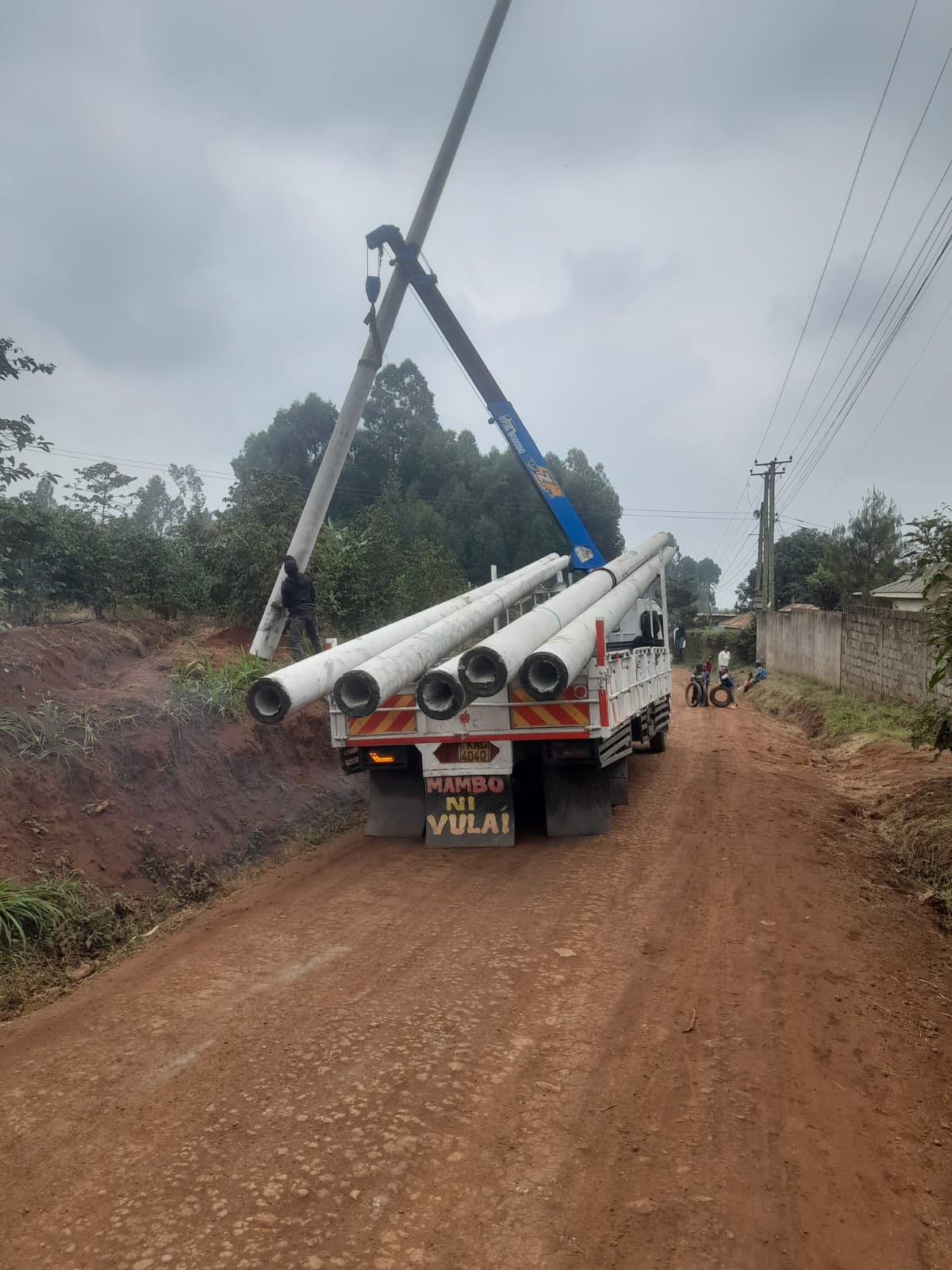 Lighting poles being offloaded from a truck along a ward road