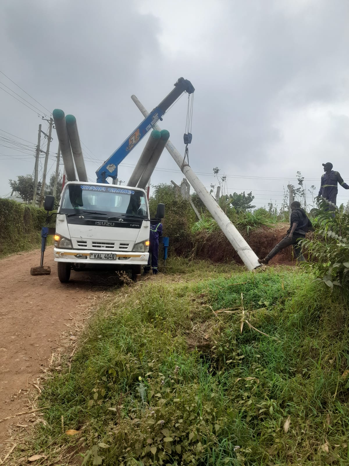 Crane truck lowering a lighting pole into position beside a ward road