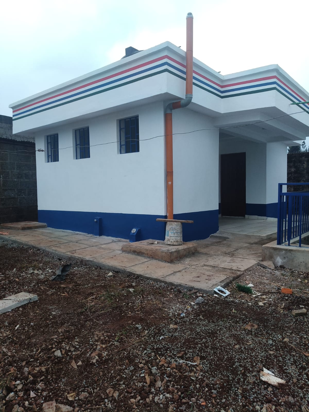 Corner view of a completed dispensary block with roof plumbing and paved apron