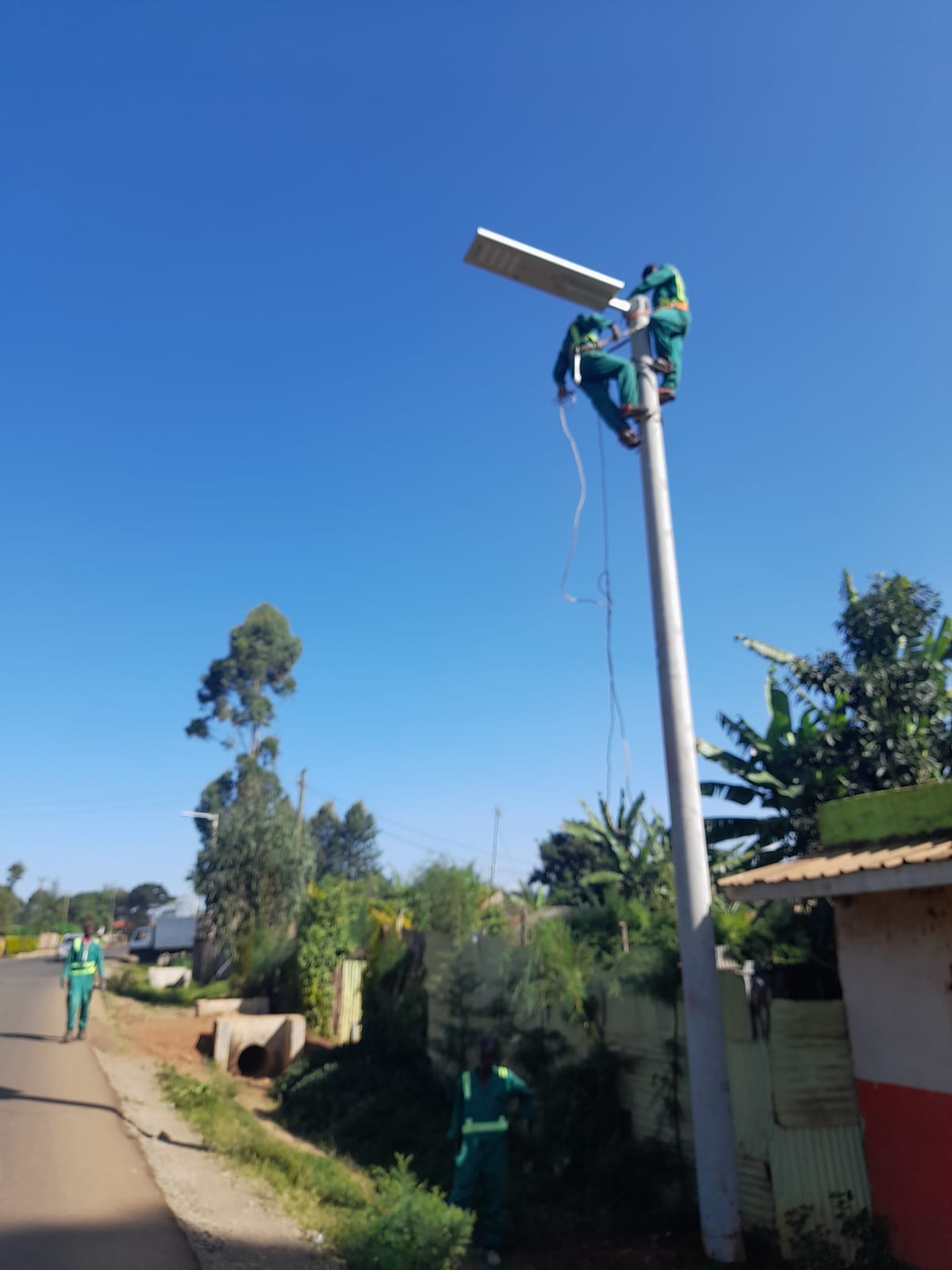 Technicians servicing a solar streetlight fitting on a mast in Githunguri Ward